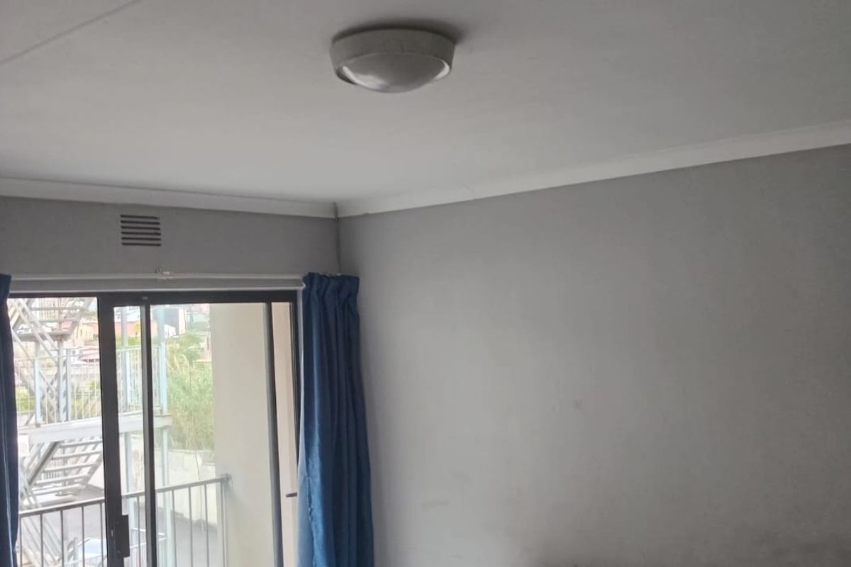A simple, empty bedroom featuring neutral grey walls, a ceiling light fixture, and a sliding glass door providing access to an outdoor balcony.