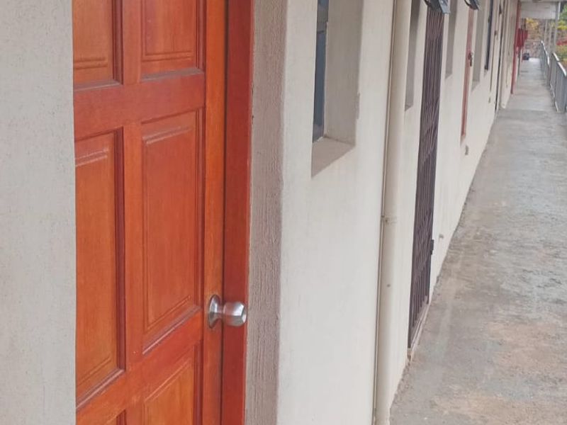 Exterior apartment hallway featuring timber entrance doors, concrete flooring, and metal balustrades along the walkway.