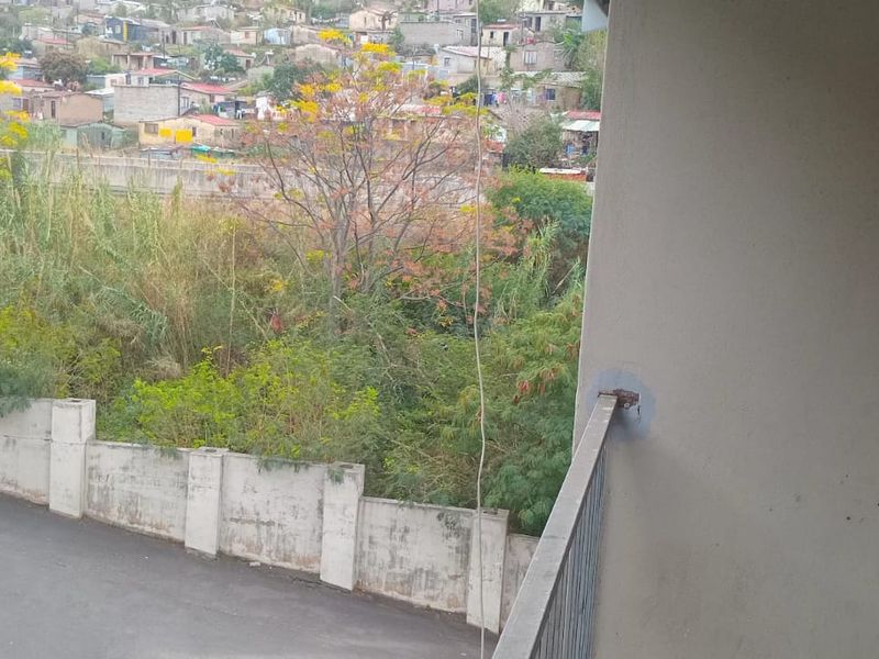 A balcony view overlooking a paved area, boundary wall, and surrounding neighborhood landscape.