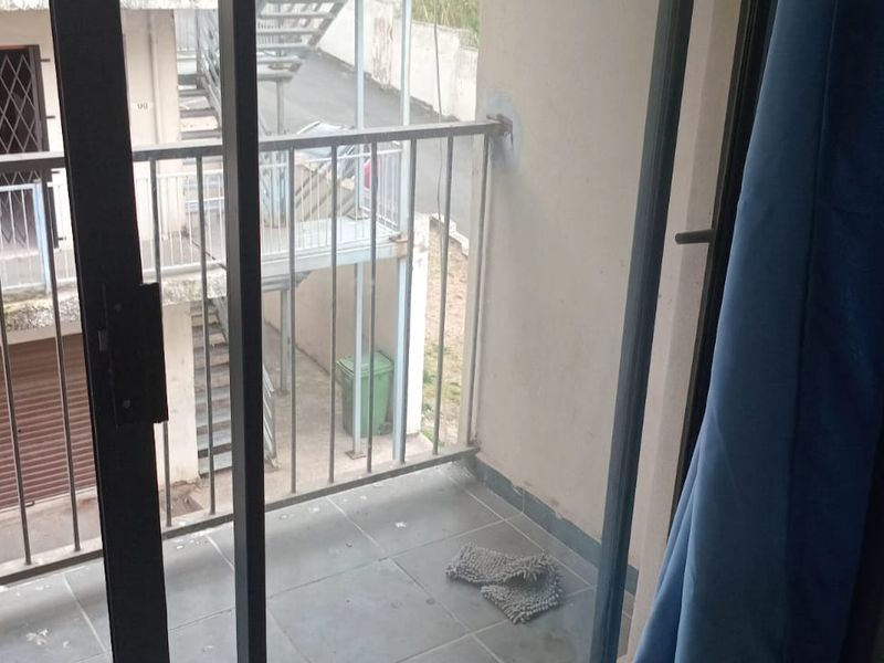 A compact balcony featuring tiled flooring and a metal balustrade, offering an outdoor space accessible via a sliding glass door.