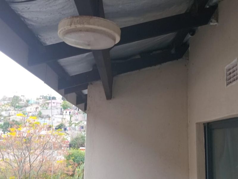 A covered balcony area featuring exposed steel roof beams and a view of the surrounding neighborhood.