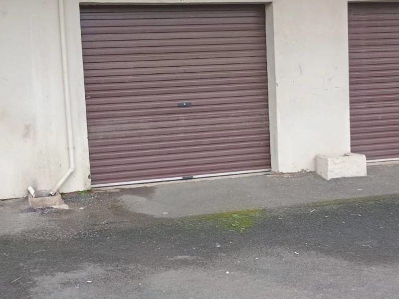 Exterior view of a residential garage with a roller shutter door, featuring an overhead balcony with a metal balustrade.