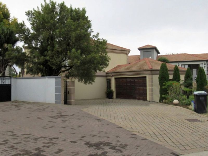 Front exterior view of the property featuring a paved driveway, double garage, and secure perimeter wall with gated access.