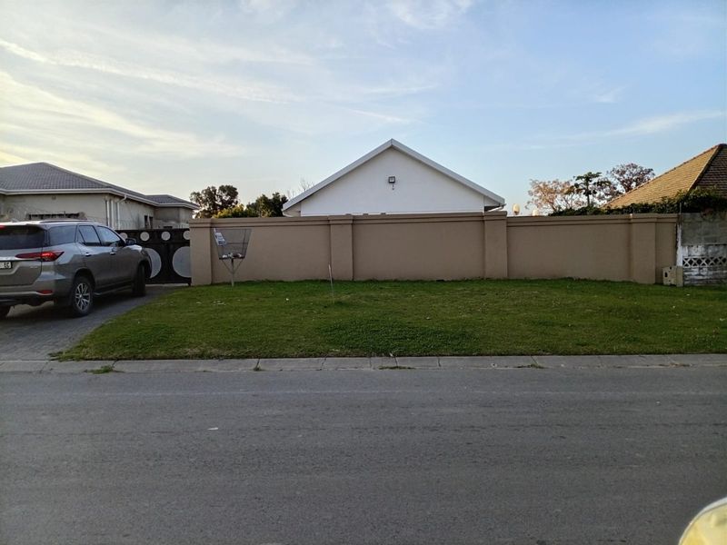 Street view of the property showing a paved driveway, front lawn, and a solid perimeter wall with a security light.