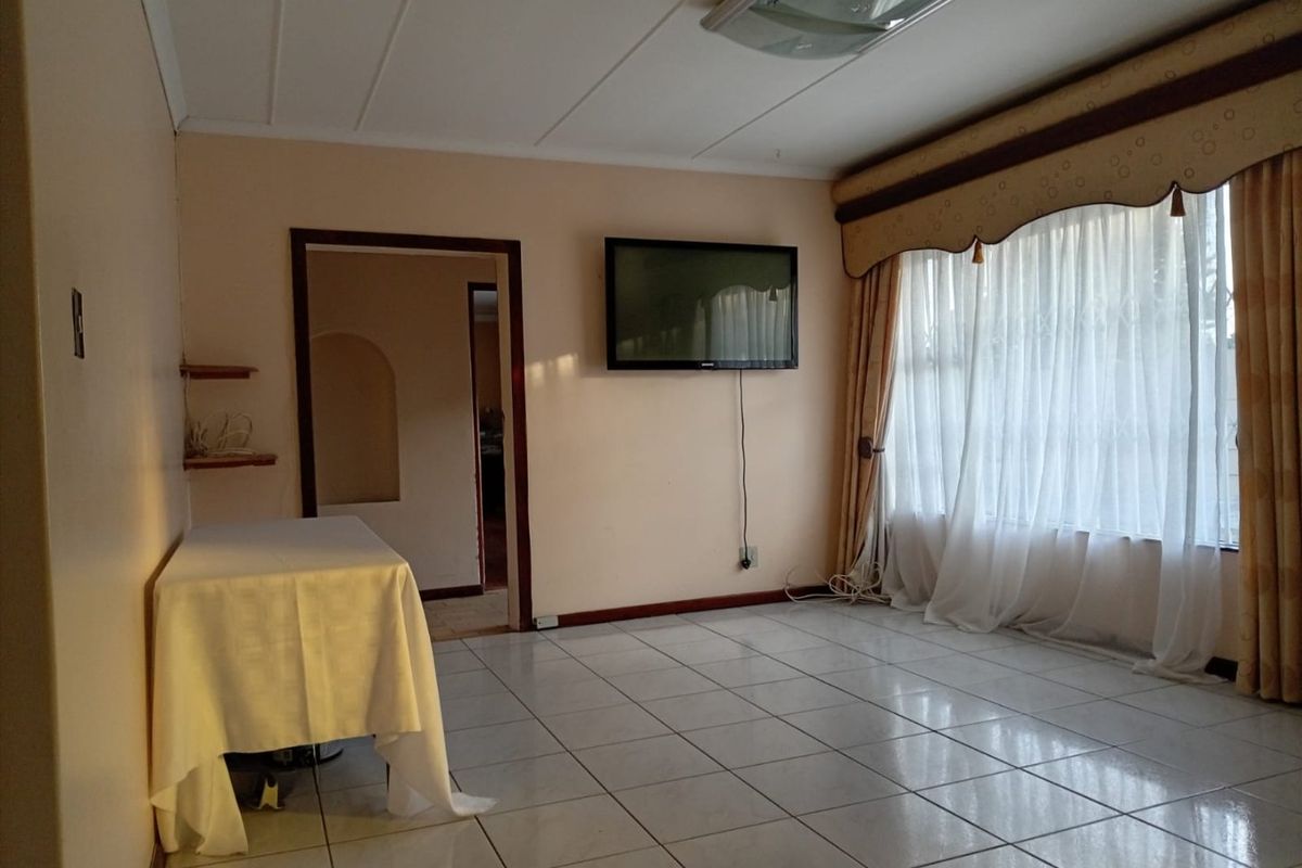 A spacious living room featuring neutral tiled flooring, an archway leading to adjacent areas, and large windows with classic drapery.