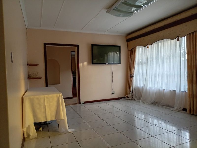 A spacious living room featuring neutral tiled flooring, an archway leading to adjacent areas, and large windows with classic drapery.