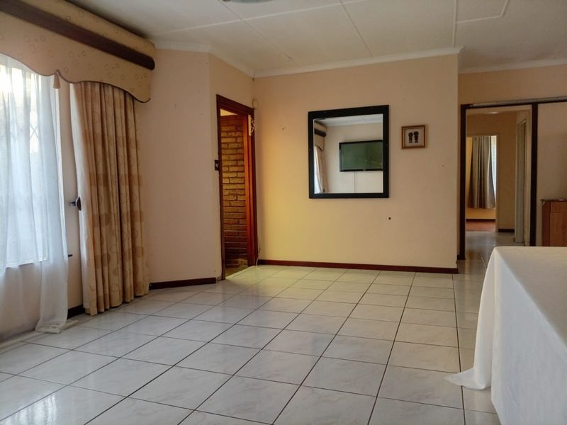 A spacious, empty living area featuring neutral ceramic floor tiles, coved ceilings, and an exposed brick doorway leading to an adjacent room.