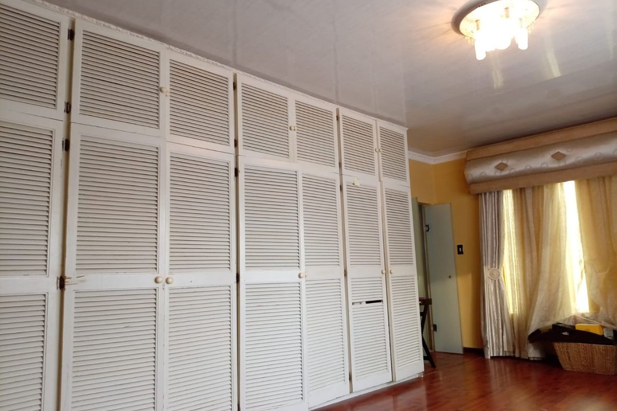 Bedroom featuring extensive floor-to-ceiling built-in cupboards with louvered doors and polished hardwood flooring.