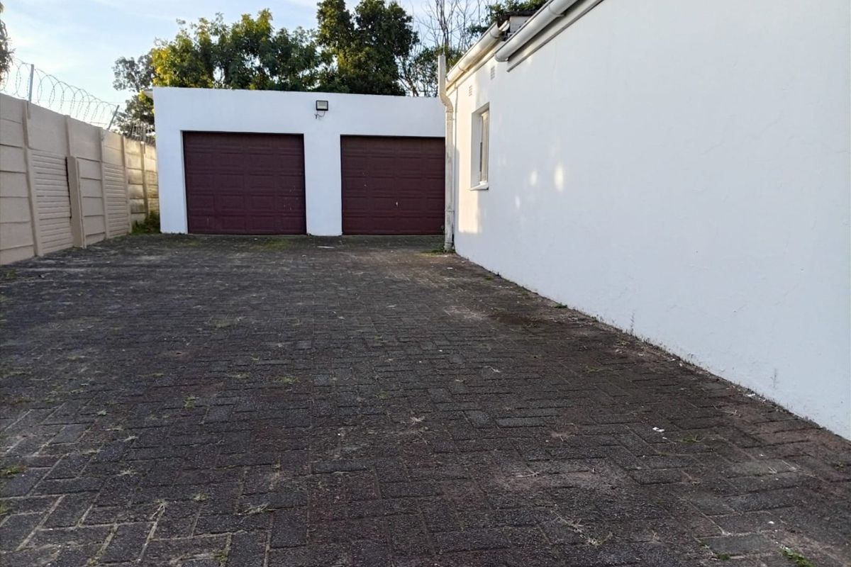 Rear exterior view featuring a double garage with paved driveway and secure boundary walling.