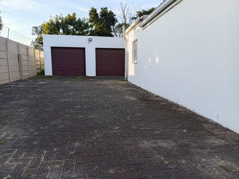 Rear exterior view featuring a double garage with paved driveway and secure boundary walling.