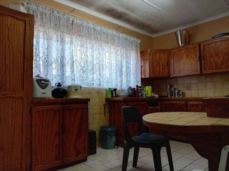 A dated kitchen featuring wooden cabinetry, tiled backsplash, and tiled flooring, showing signs of ceiling water damage and requiring cosmetic updates.
