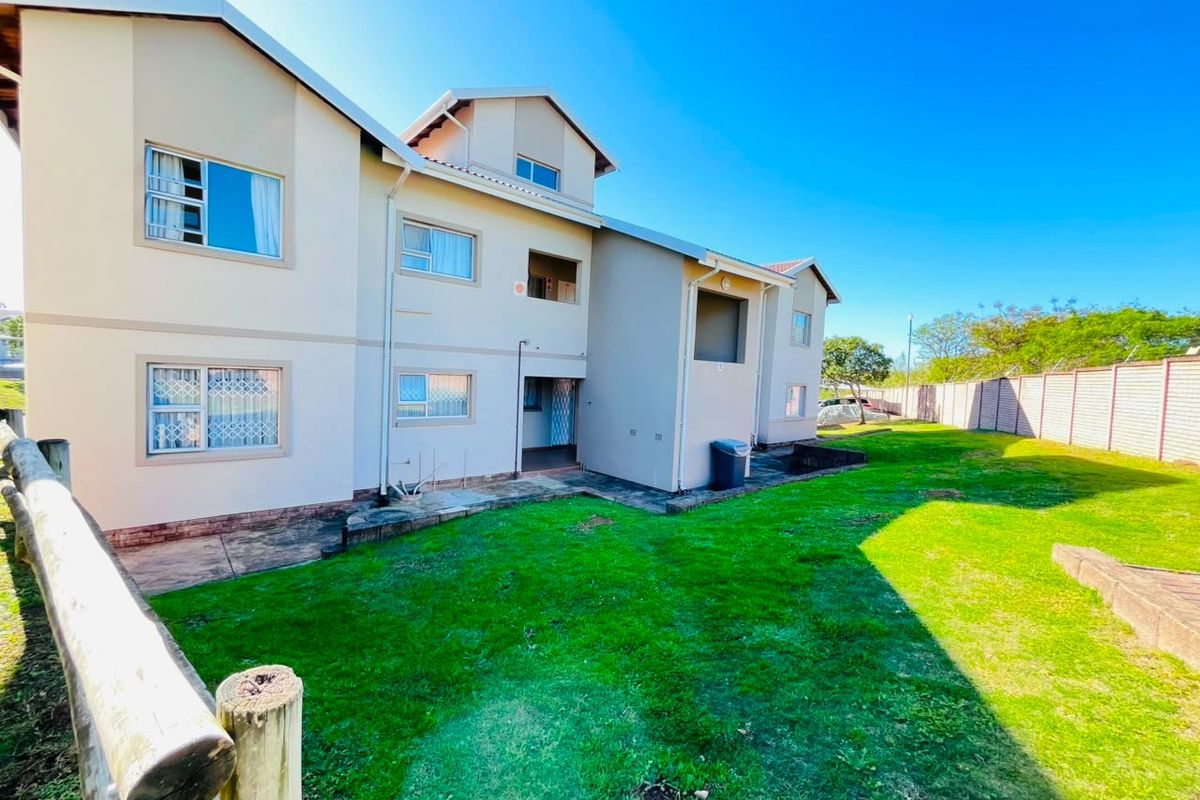 Rear view of the apartment complex featuring a shared lawn area, paved walkways, and exterior building facade with security-fitted windows.