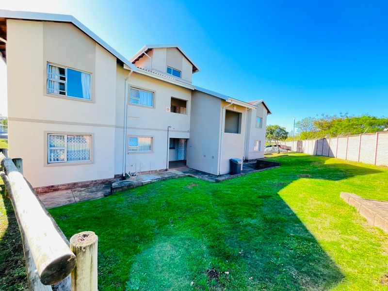 Rear view of the apartment complex featuring a shared lawn area, paved walkways, and exterior building facade with security-fitted windows.