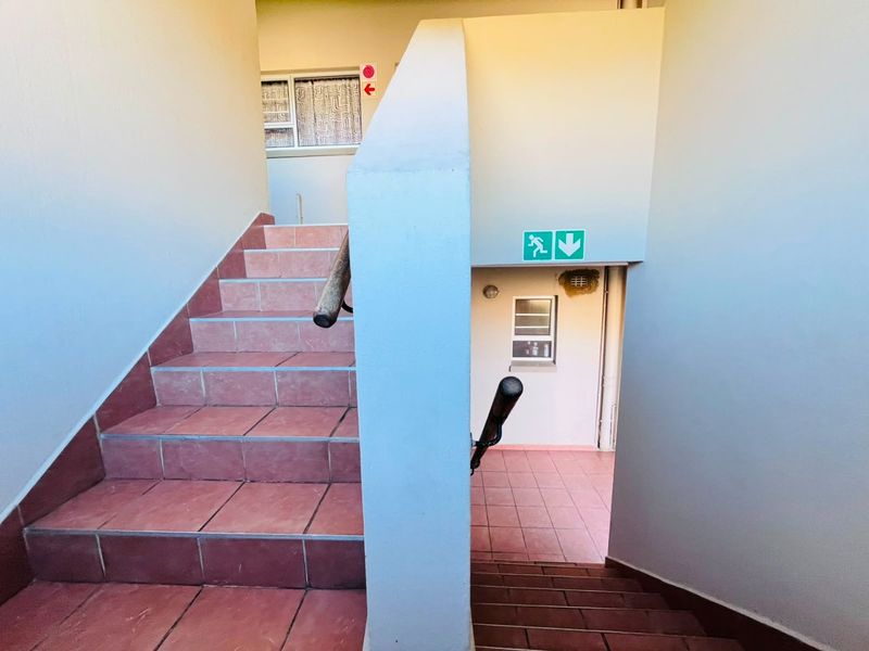 A functional apartment building stairwell featuring tiled steps, handrails, and emergency exit signage.