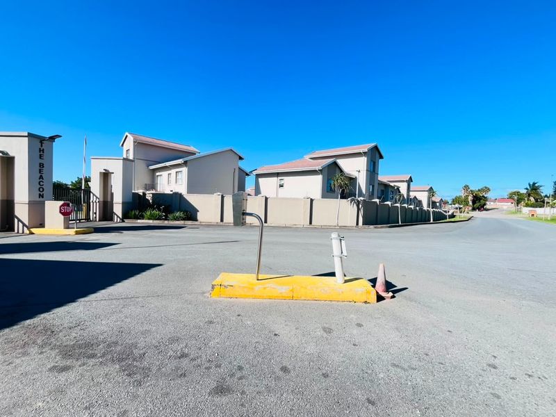 Street view of the entrance to The Beacon apartment complex, featuring perimeter walls, security access control, and paved driveway access.