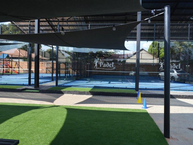 A well-maintained commercial padel court facility featuring glass enclosures, artificial turf surfaces, and overhead shade sails for outdoor play.