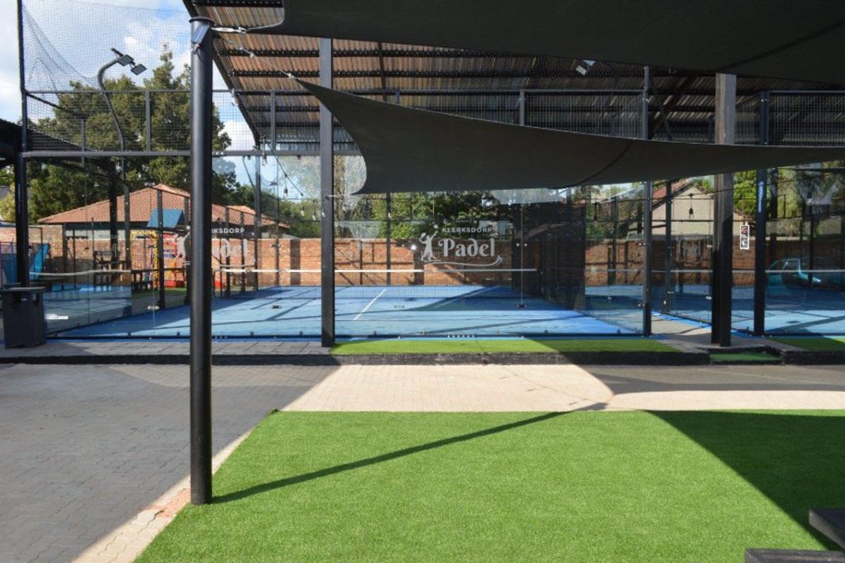 A well-maintained commercial padel court facility featuring glass walls, metal roofing, artificial turf surfacing, and integrated shade sails for outdoor play.