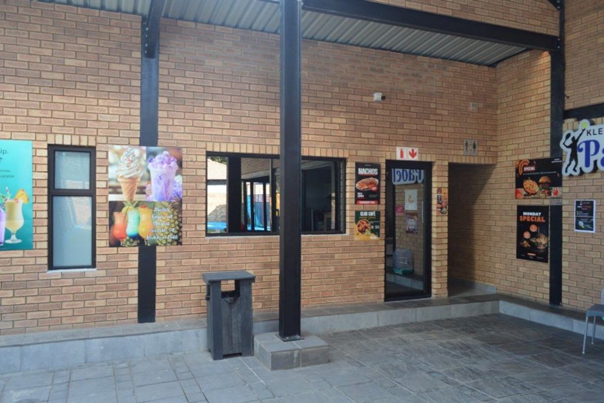 A commercial exterior patio area featuring face brick walls, steel structural columns, and paved flooring, providing access to the building interior.