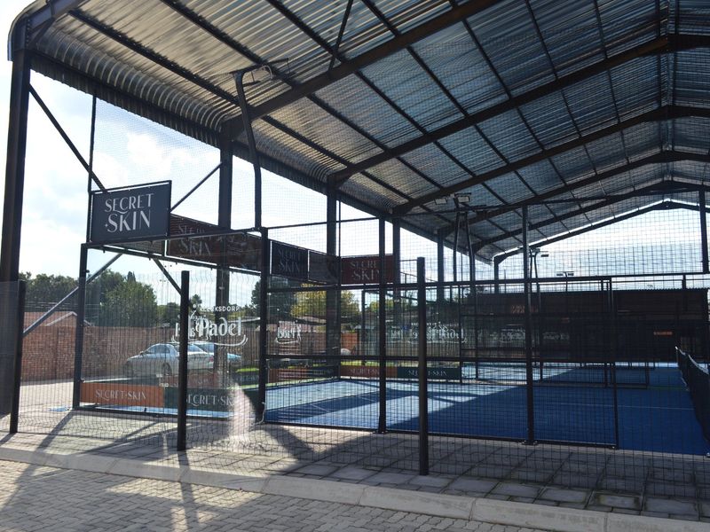 A well-maintained covered padel court facility featuring a steel frame structure, wire mesh enclosure, and professional synthetic court surface.