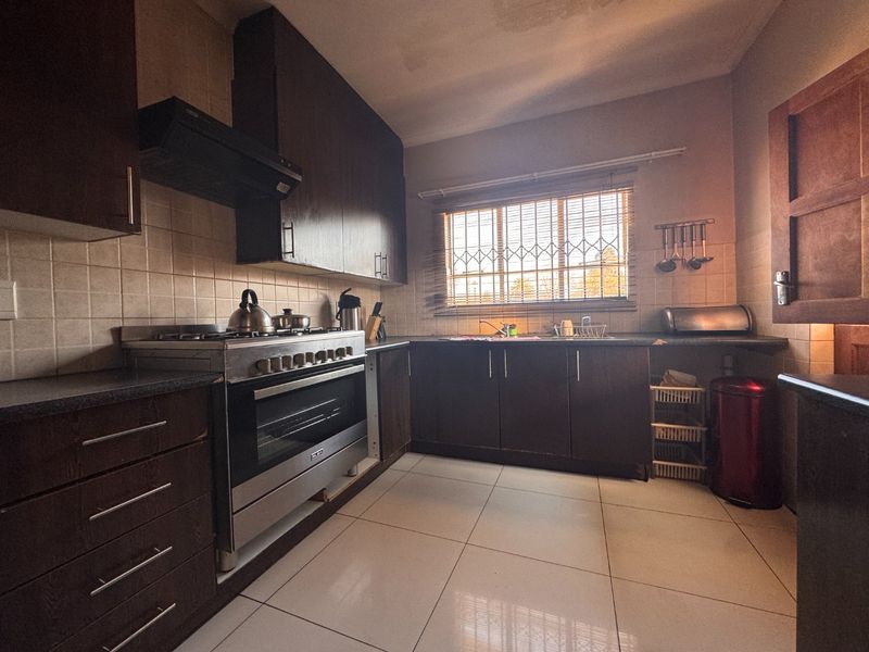 Functional kitchen featuring dark wood cabinetry, stainless steel gas stove, tiled flooring, and a tiled backsplash with security bars on the window.