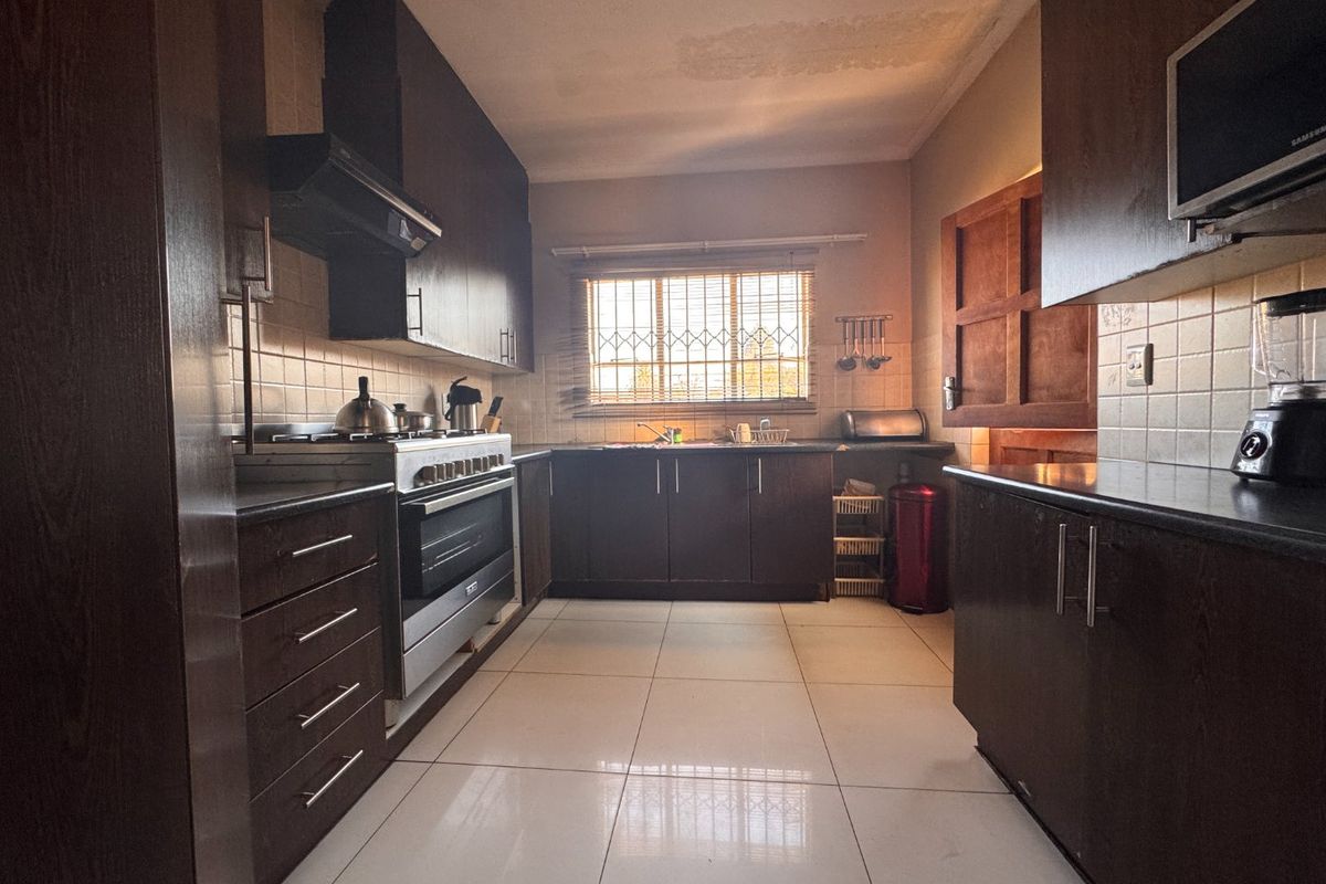 A functional kitchen featuring dark wood cabinetry, built-in oven, gas hob, and tiled finishes, with visible ceiling staining requiring attention.