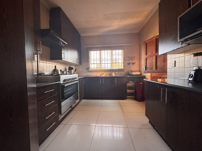 A functional kitchen featuring dark wood cabinetry, built-in oven, gas hob, and tiled finishes, with visible ceiling staining requiring attention.