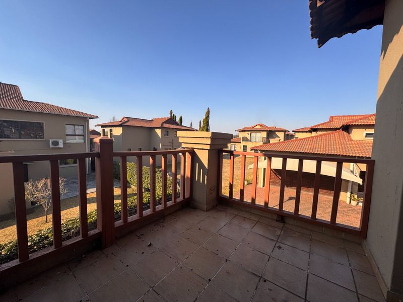 An elevated balcony with tiled flooring and a wooden balustrade, offering views over the surrounding residential estate.