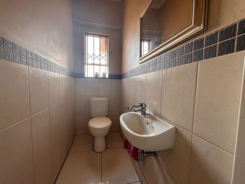 A compact guest bathroom featuring a wall-mounted basin, toilet, and neutral tiled finishes with a decorative border.