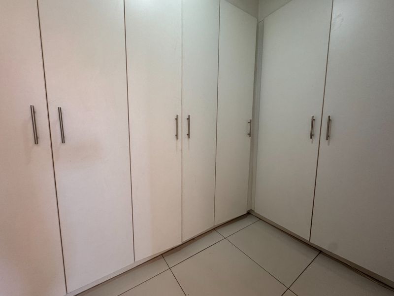 A clean bedroom interior featuring floor-to-ceiling built-in cupboards and neutral tiled flooring, offering ample storage space.