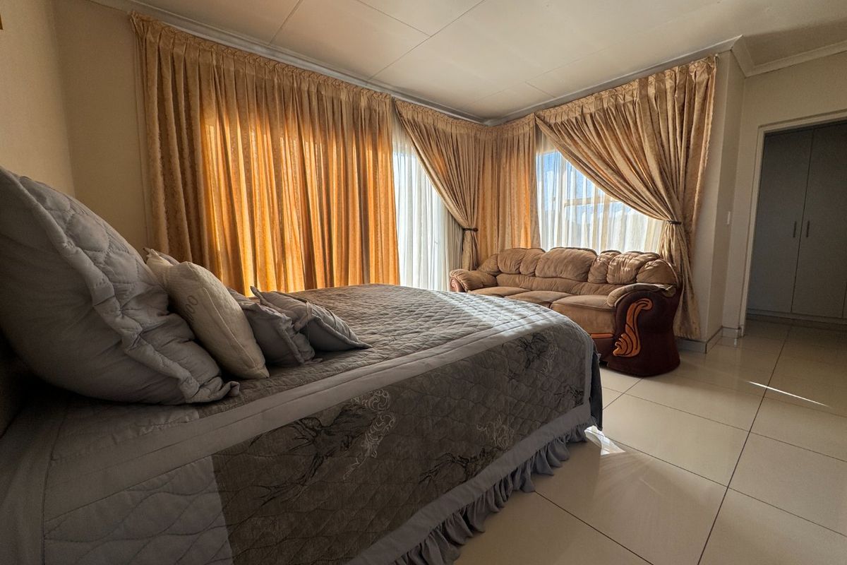 Spacious bedroom featuring large windows with floor-to-ceiling curtains, tiled flooring, and built-in storage cupboards.