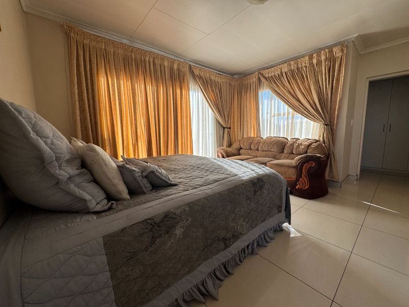Spacious bedroom featuring large windows with floor-to-ceiling curtains, tiled flooring, and built-in storage cupboards.