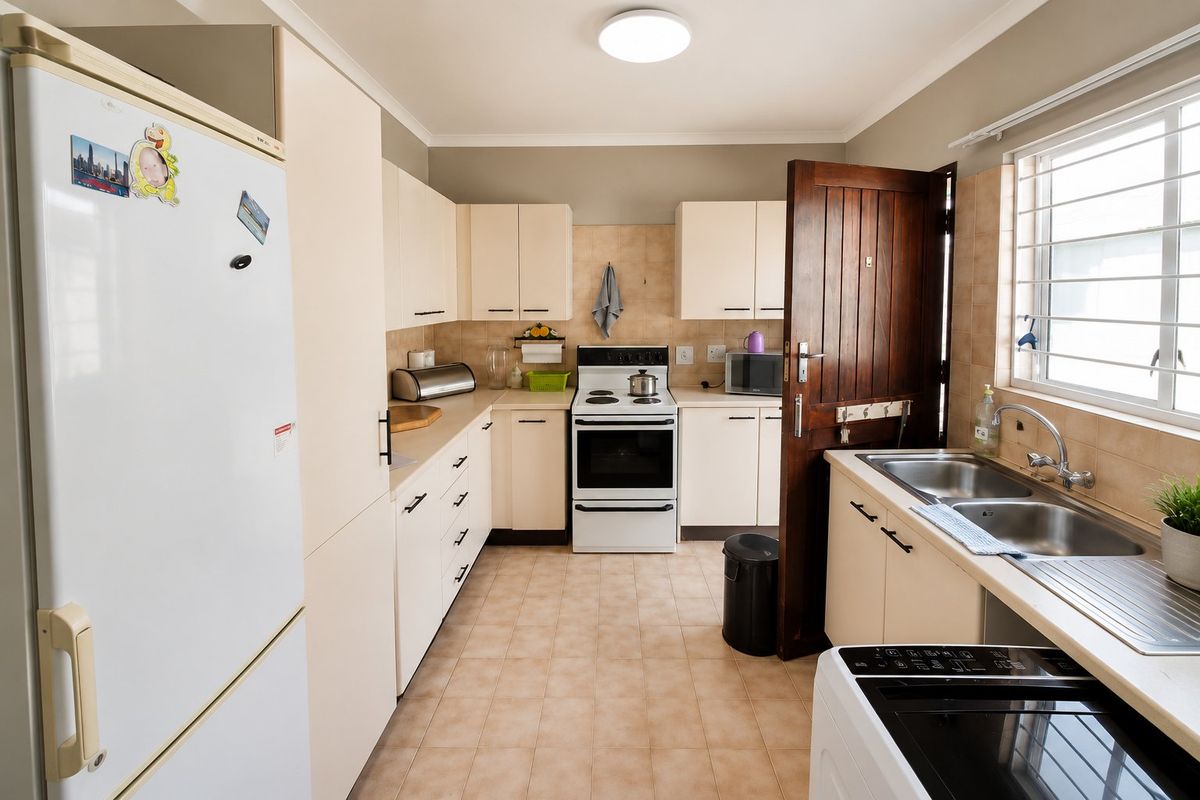 Functional kitchen featuring light-toned cabinetry, tiled backsplash, double basin sink, and a freestanding stove, offering a practical layout with natural light.
