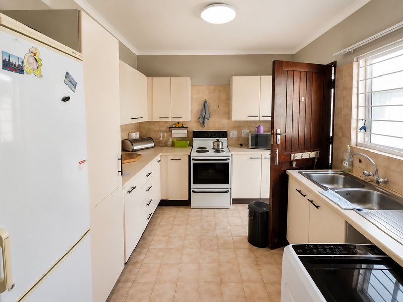Functional kitchen featuring light-toned cabinetry, tiled backsplash, double basin sink, and a freestanding stove, offering a practical layout with natural light.