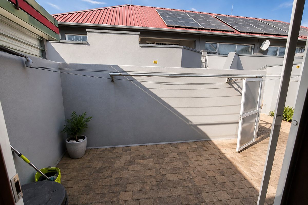 A private paved rear courtyard featuring a wall-mounted clothesline and secure boundary walling, with solar panels visible on the roof above.