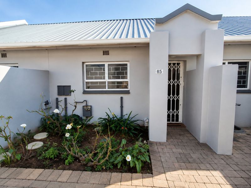 Front entrance of a townhouse featuring a paved walkway, security gate, and well-maintained exterior facade with a metal roof.