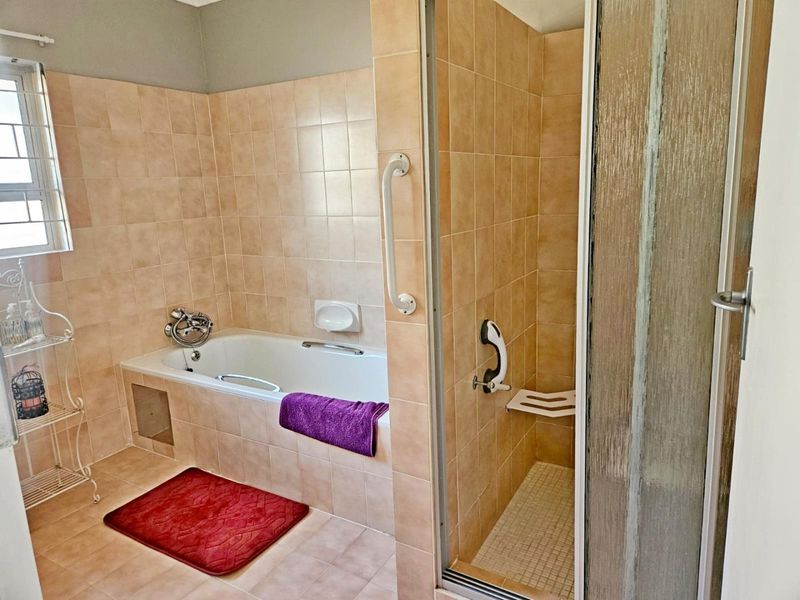 A functional bathroom featuring a built-in bathtub, separate shower enclosure with grab rails, and neutral wall tiling.