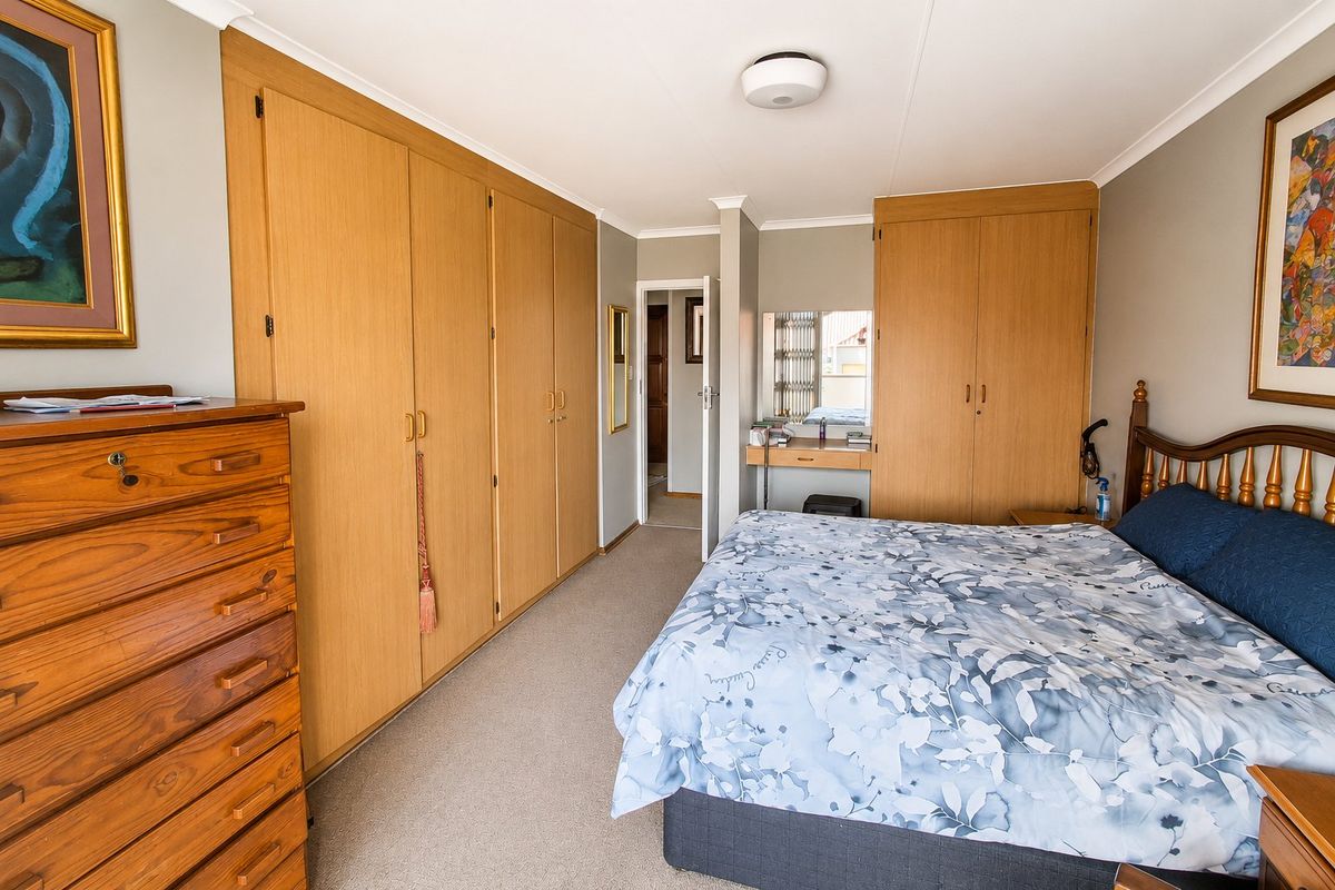 Spacious bedroom featuring extensive built-in wooden cupboards, a dedicated vanity area, neutral carpeting, and coved ceilings.