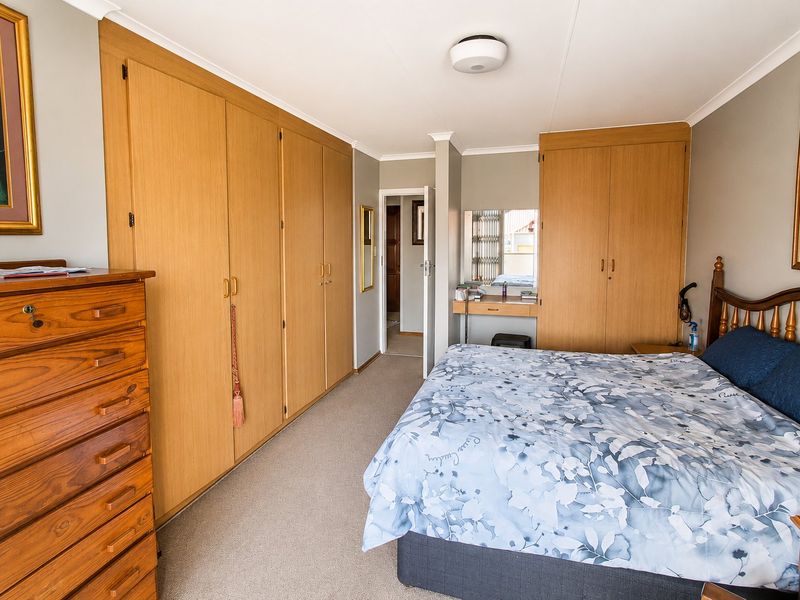 Spacious bedroom featuring extensive built-in wooden cupboards, a dedicated vanity area, neutral carpeting, and coved ceilings.