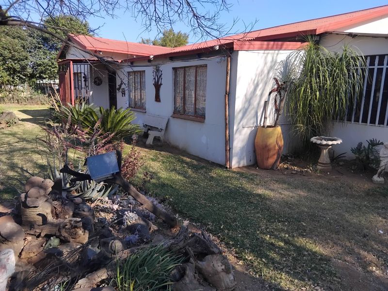 Front elevation of a single-story house featuring a corrugated metal roof, security bars on windows, and a landscaped garden area.