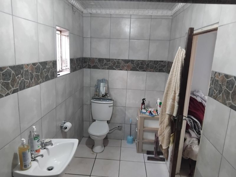 A functional bathroom featuring ceramic wall and floor tiles, a standard pedestal basin, and a toilet, requiring minor maintenance and cosmetic updates.