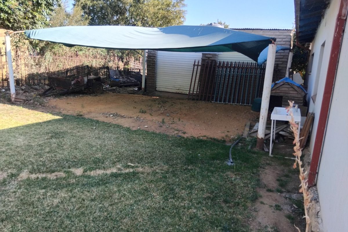 Rear yard area featuring a shade sail, lawn, and detached garage structure with an outdoor utility sink.
