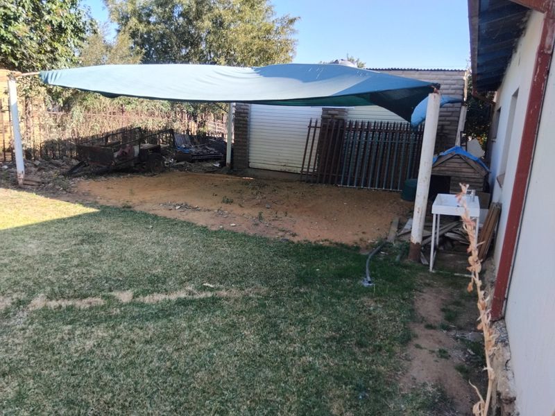 Rear yard area featuring a shade sail, lawn, and detached garage structure with an outdoor utility sink.