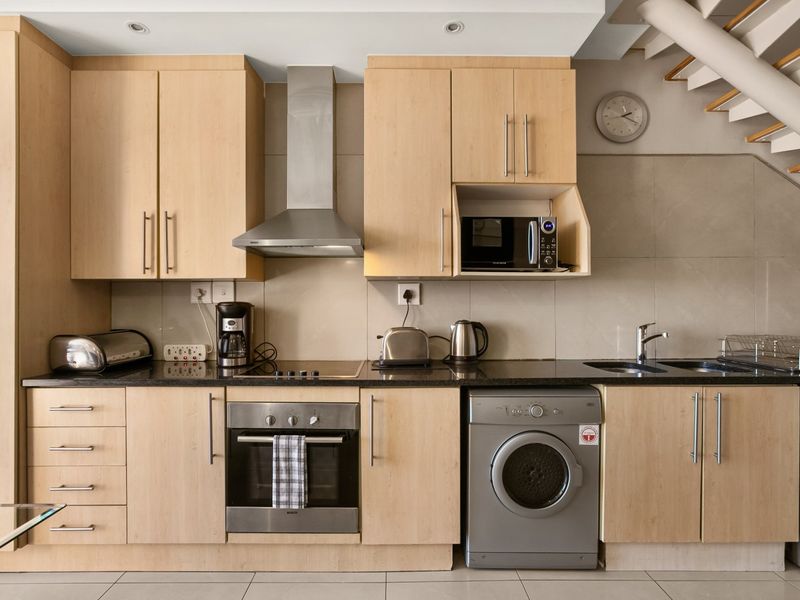 Modern kitchen featuring light-wood cabinetry, granite countertops, integrated stainless steel appliances, and a tiled backsplash, conveniently located beneath a staircase.