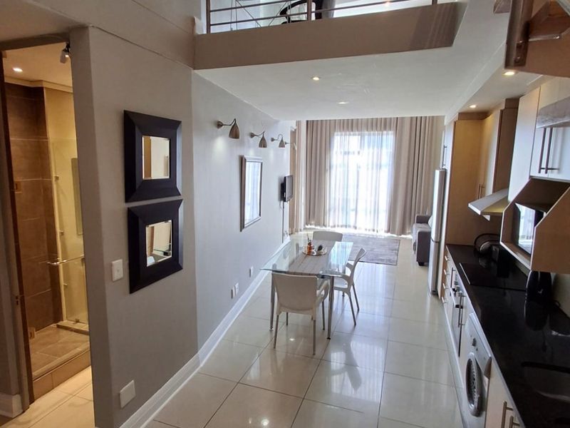 Modern open-plan apartment featuring a sleek kitchen with granite countertops, tiled flooring, and a mezzanine level with a metal balustrade overlooking the living area.