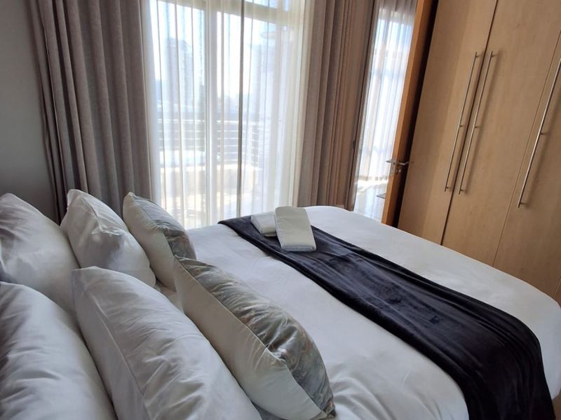 A well-maintained bedroom featuring built-in wooden wardrobes, recessed ceiling lighting, and large sliding glass doors that provide ample natural light.