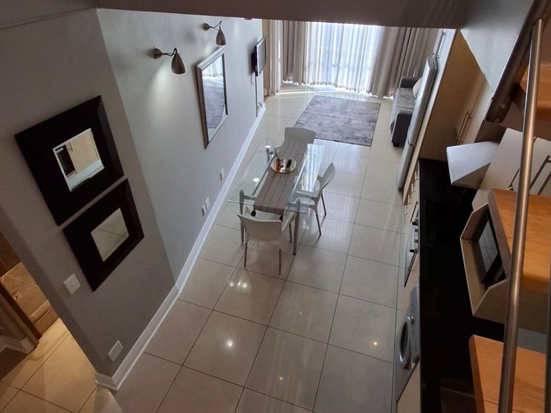 An open-plan living and dining area featuring tiled floors, a modern staircase with metal railings, and a functional kitchen layout with built-in cabinetry.