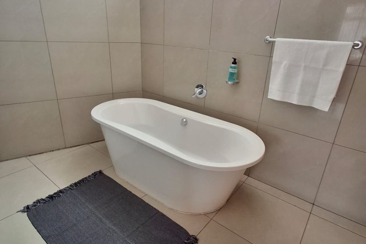 Modern bathroom featuring a sleek freestanding bathtub, neutral large-format ceramic wall and floor tiles, and a wall-mounted faucet.