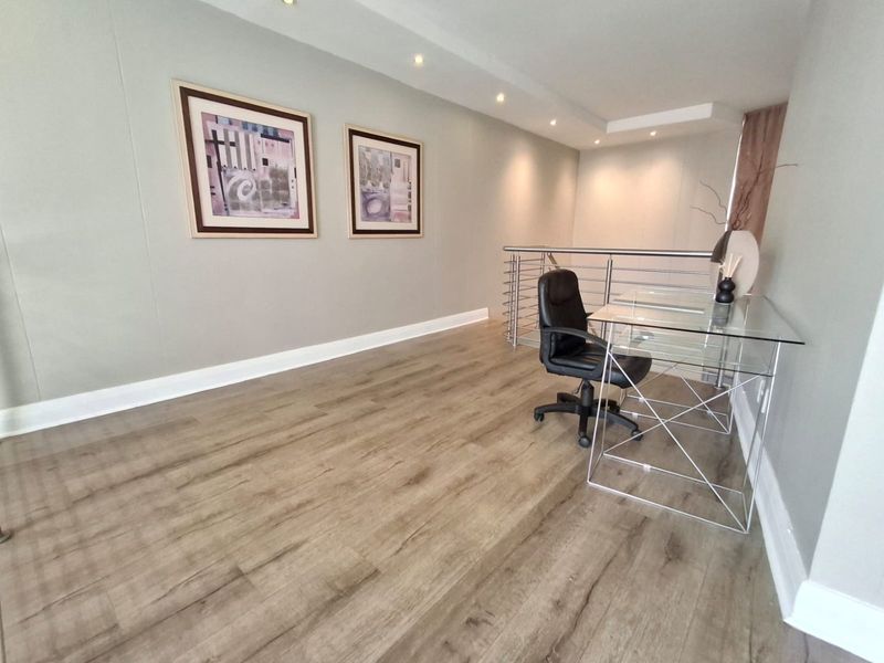 A bright, open-plan office space featuring modern laminate flooring, recessed ceiling lighting, and a sleek stainless steel balustrade overlooking the lower level.