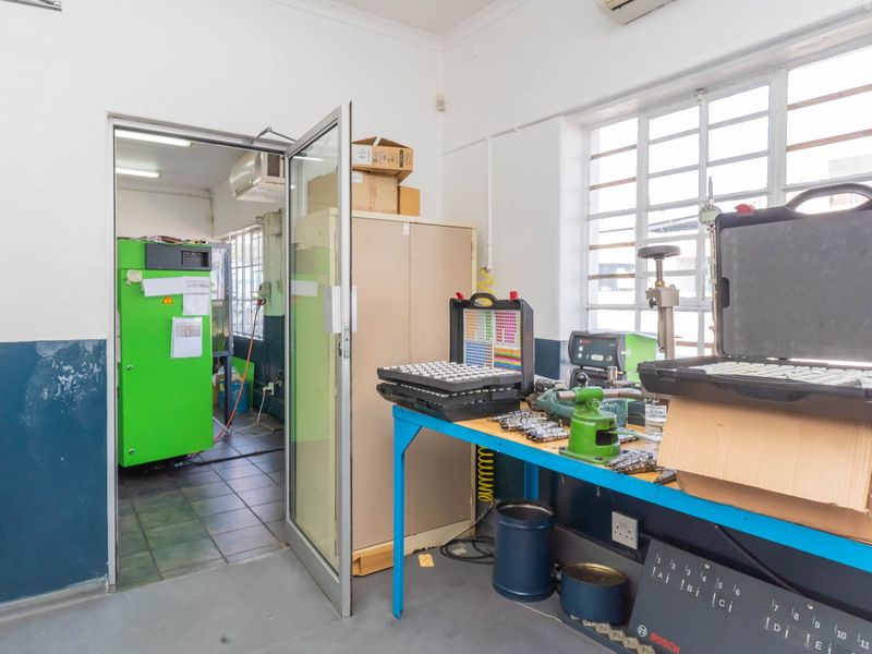Industrial utility space featuring tiled flooring, large steel-framed windows, and an integrated air conditioning unit, suitable for workshop or technical operations.