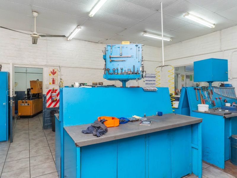 Industrial workshop space featuring built-in blue metal workbenches, tiled flooring, fluorescent lighting, and functional utility infrastructure.